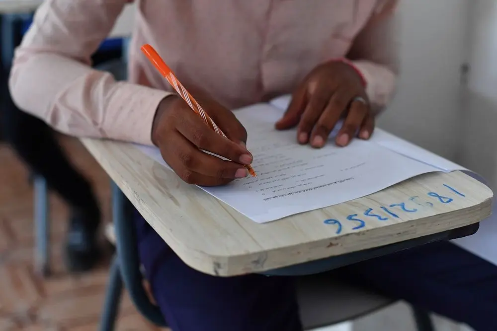 Student writing answers on an exam paper at a classroom desk during a test.
