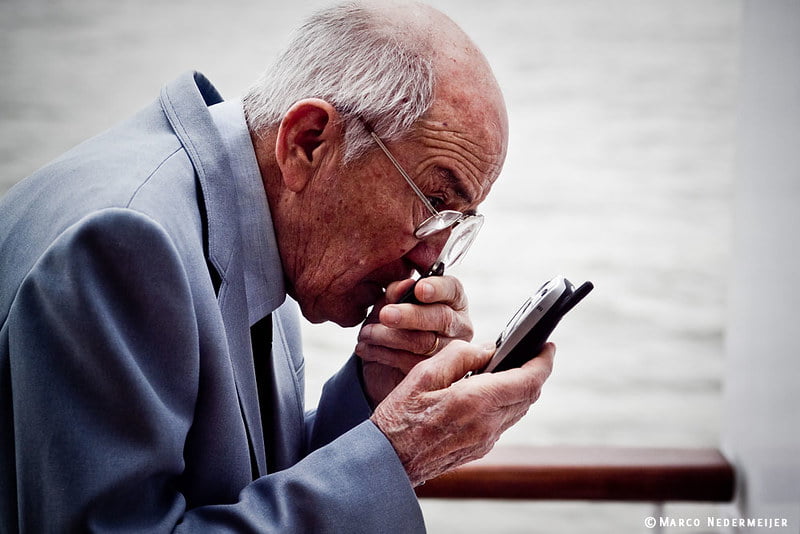 An old man trying to dial a phonenumber on his cellphone.