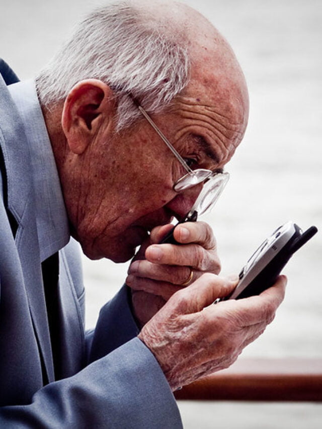 An old man trying to dial a phonenumber on his cellphone.