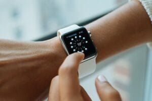 Person wearing an Apple Watch with digital interface visible on the screen, showing app icons against a white background.