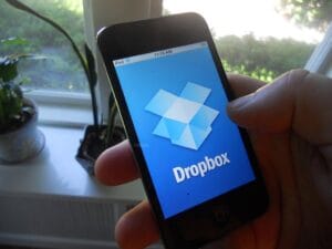 A hand holding a smartphone displaying the Dropbox logo on screen.