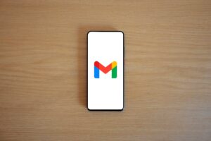 Smartphone displaying Gmail logo on white screen against wooden surface background