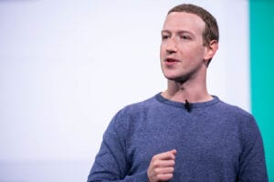 Mark Zuckerberg speaking at Facebook's F8 Developer Conference in 2019, wearing a blue sweater against a teal background.