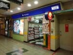 Exterior of a PlayStation retail shop in a brightly lit mall corridor with blue PlayStation signage and shelves of game cases.
