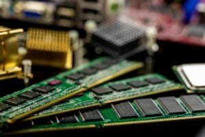 Close-up of a green circuit board memory module (RAM) with black heat spreader against a dark background, showing the intricate electronic components and gold contacts.
