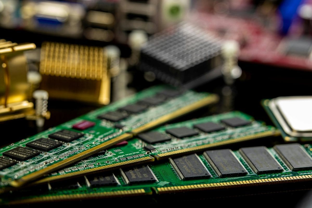 Close-up of a green circuit board memory module (RAM) with black heat spreader against a dark background, showing the intricate electronic components and gold contacts.