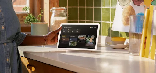 Google Nest Hub smart display on kitchen countertop showing the Google Home interface with photo gallery feature, surrounded by kitchen items including a glass vase and wooden canister.