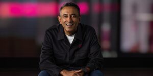 Srini Gopalan smiling in black T-Mobile branded jacket against blurred magenta background