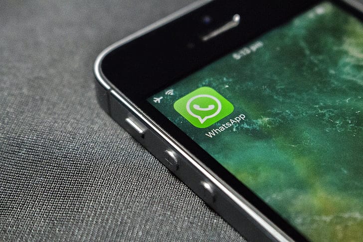 iPhone displaying WhatsApp application icon on screen against gray fabric background.