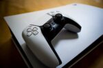 Close-up of a white DualSense controller placed on a PlayStation 5 console in soft ambient light.
