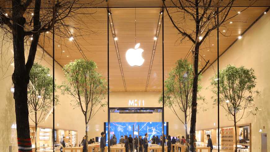 Apple retail store front exterior with glass facade and illuminated Apple logo showing company's physical retail infrastructure