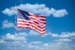 American flag waving against clear blue sky symbolizing national security concerns over massive government contractor data breach affecting millions of US citizens