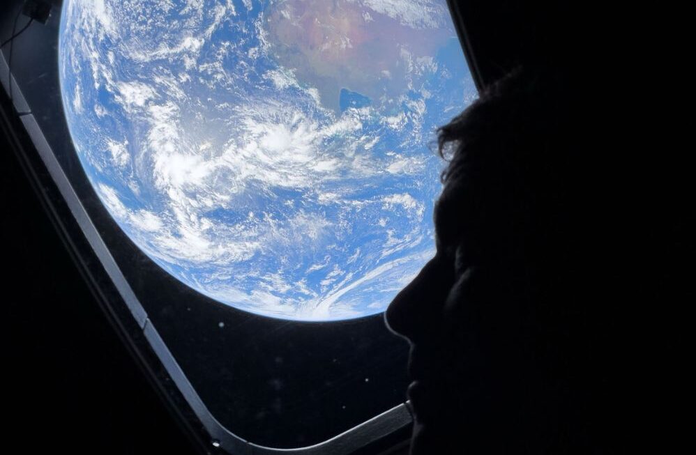 Earth photographed from the Orion spacecraft window by NASA Artemis II Commander Reid Wiseman on April 3 2026 showing the full disk of Earth at night lit by moonlight with two auroras and the African continent visible