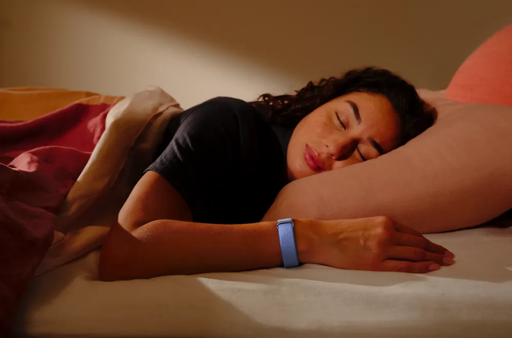 Woman sleeping while wearing the Fitbit Air Performance Loop band in Lavender on her wrist