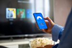 Person holding a smartphone displaying a VPN connection screen while sitting in front of a smart TV at home