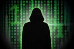 A stylized illustration of a hooded hacker figure sitting at a computer, representing the archetypal image of a cyber attacker.