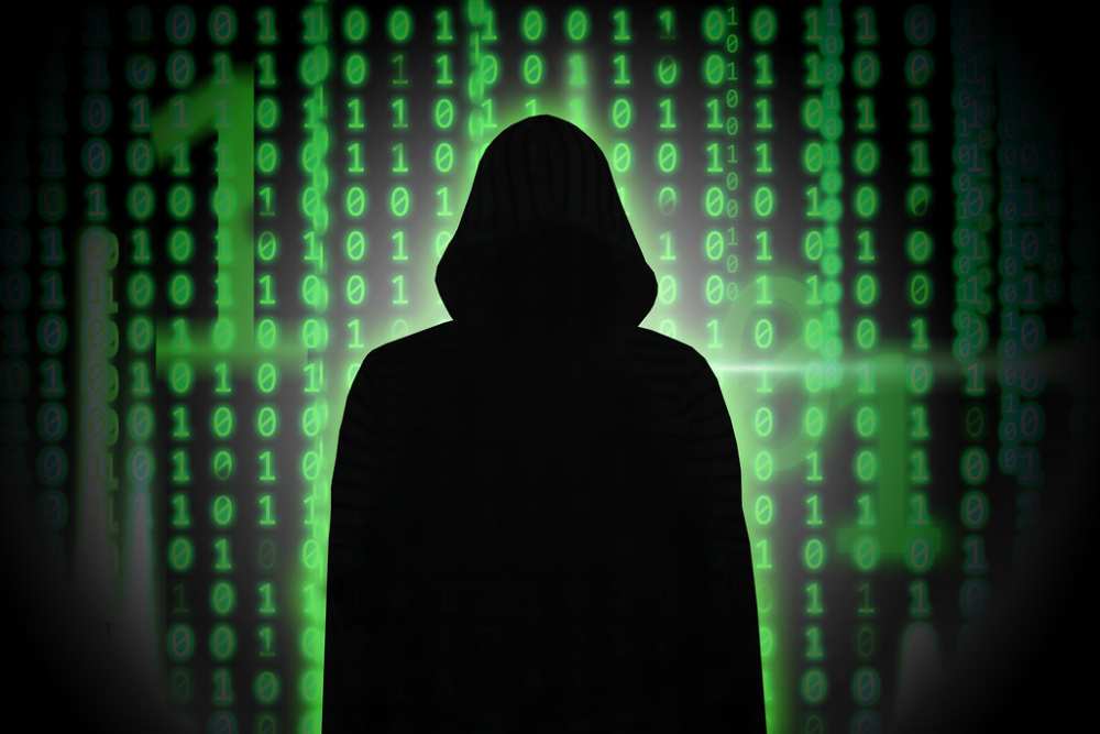 A stylized illustration of a hooded hacker figure sitting at a computer, representing the archetypal image of a cyber attacker.