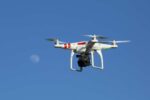 A DJI Phantom drone with a GoPro camera mounted underneath, flying against a blue sky with the moon visible in the background