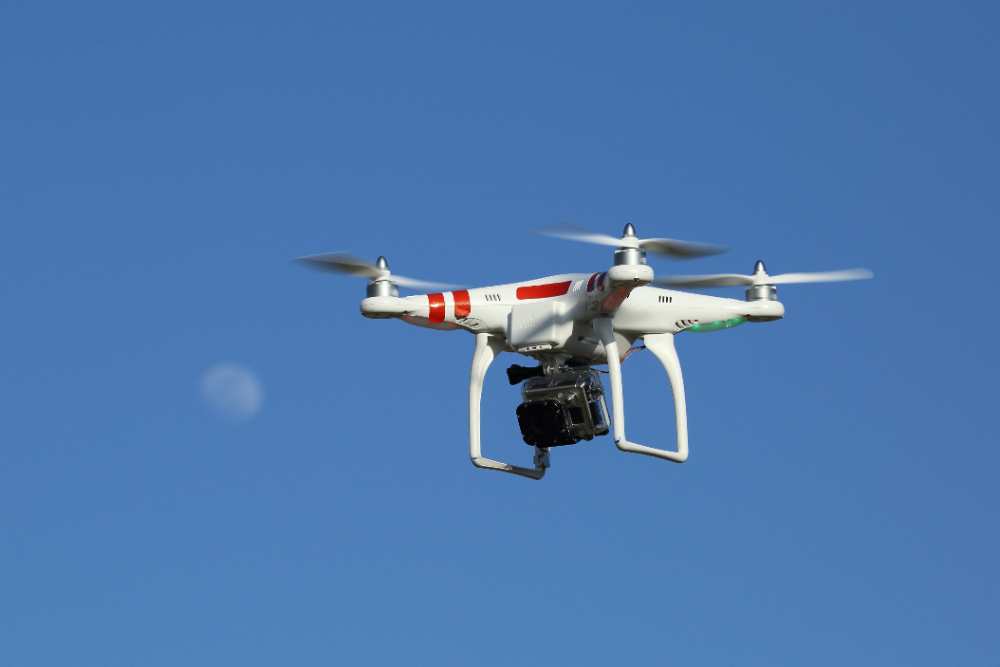 A DJI Phantom drone with a GoPro camera mounted underneath, flying against a blue sky with the moon visible in the background